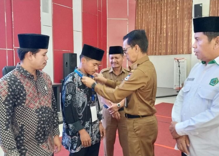 Asisten I Sekretaris Daerah Kota (Setdako) Padang, Edi Hasymi saat mengalungkan tanda peserta Master of Trainer (MoT) yang dilaksanakan di Balaikota Padang, Senin (10/2/2025). (Foto: Diskominfo Padang)