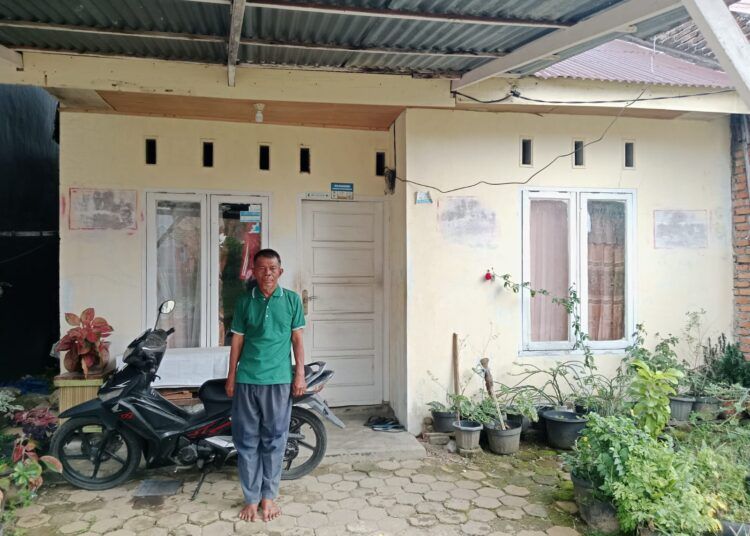 Syamsuir (66 tahun) atau Win berdiri di depan rumah subsidinya di Perumahan Kandis Asri Nomor J2, Kelurahan Aia Pacah, Kecamatan Koto Tangah, Kota Padang, Sumatera Barat, pada Rabu (11/2/2026). Foto: Qadri Hayatul/Kabarminang.com