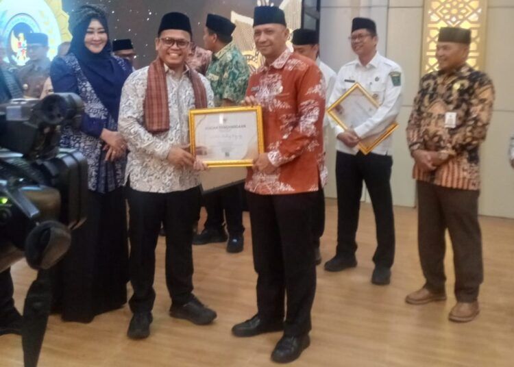 Asisten I Bidang Pemerintahan dan Kesejahteraan Rakyat Setdako Padang Panjang, I Putu Venda, mewakili wali kota menerima penghargaan dari Kemenhaj pada Jumat (31/7/2026) di Aula Asrama Haji Embarkasi Padang. Foto: Pemko Padang Panjang