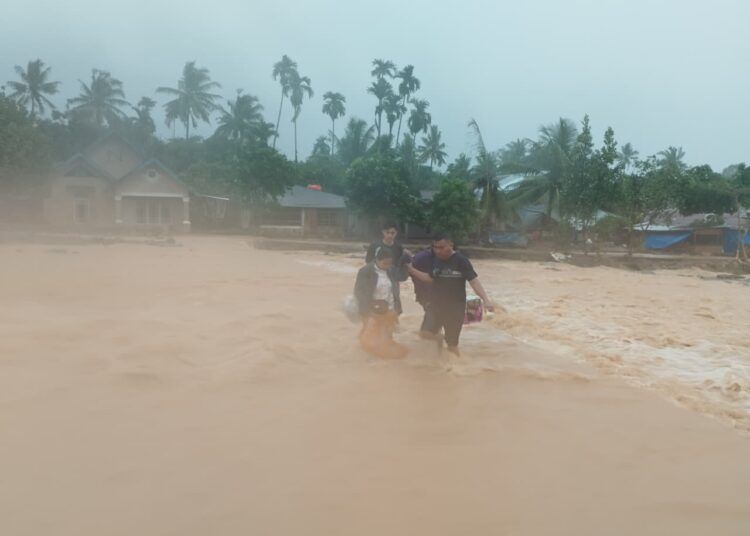 Warga mengevakuasi diri melintasi jalur yang tergenang arus deras akibat luapan Sungai Kampung Guo di kawasan Lapau Munggu, Kelurahan Kuranji, Kota Padang, Senin (3/8/2026)